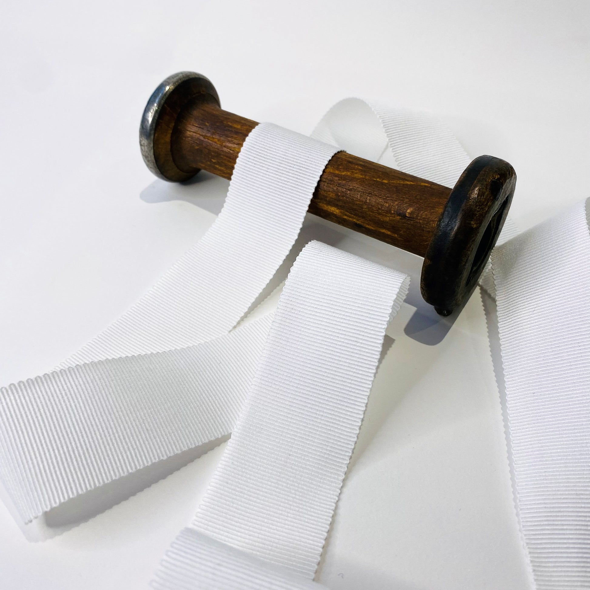 White cotton grosgrain ribbon spooled on a wooden spool, displaying various widths of the ribbon.