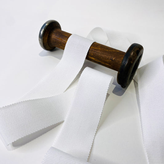 White cotton grosgrain ribbon spooled on a wooden spool, displaying various widths of the ribbon.