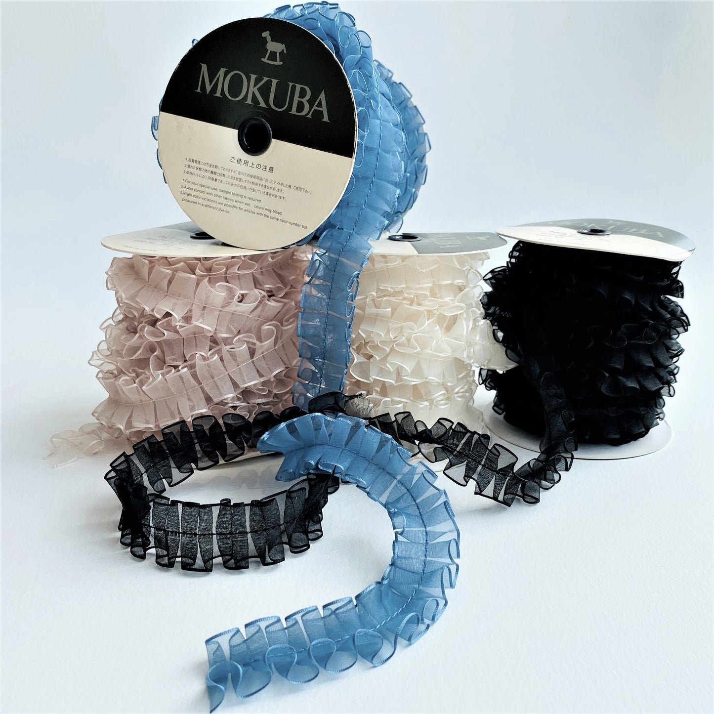 24mm Pleated Chiffon ribbon by MOKUBA A beautifully soft pleated semi-transparent sheer chiffon ribbon trim by Mokuba has been carefully pleated, held together by a single stitch running through the middle, which comes in four beautiful colours.  Col: Blue 21, Black 3, Blush 65 and Ivory 89.