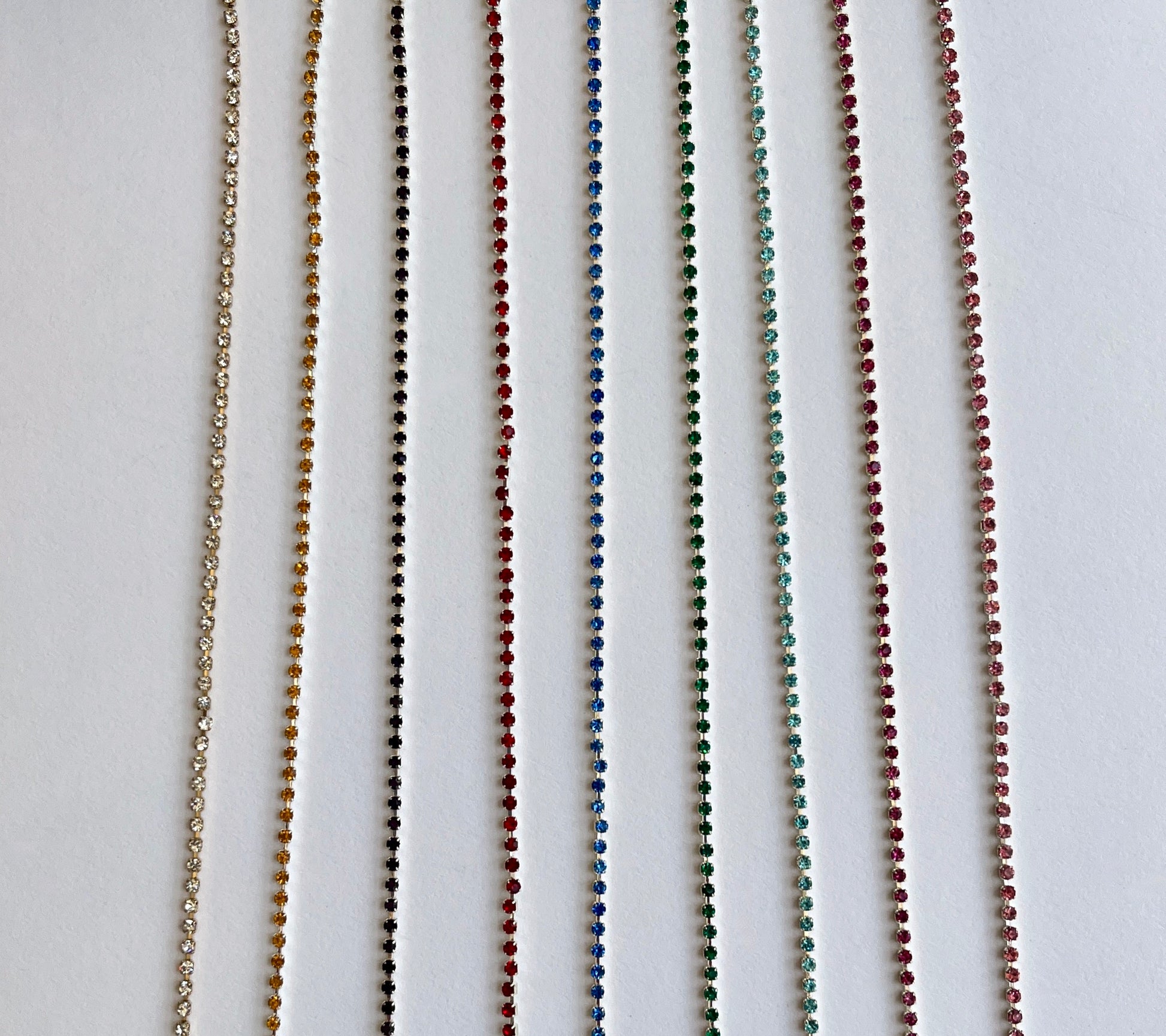 Delicate rhinsteone trim - premium high grade coloured diamante crystals set in a flexible metal chain casing  SOLD BY THE METRE Colours: gold-clear crystal, silver-saffron, silver-Amethyst (dark purple), silver-red, silver-sapphire, silver-emerald, silver-aqua, silver-fuchsia, silver-rose Approx Overall Width: 3mm (⅛”) Stone Size: SS4.5
